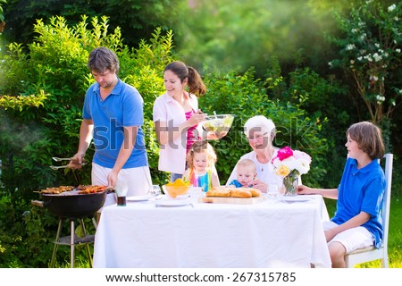 Grill barbecue backyard party. Happy family, mother, father, kids, teen son, toddler daughter and little baby, enjoying BBQ lunch with grandmother eating grilled meat in garden with salad and bread.