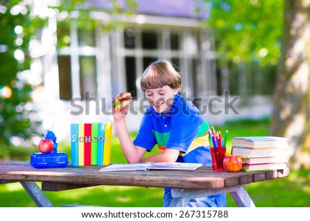 Child in school yard. Happy laughing teenager student boy in the school garden reading books and having apple for healthy snack, back to school concept