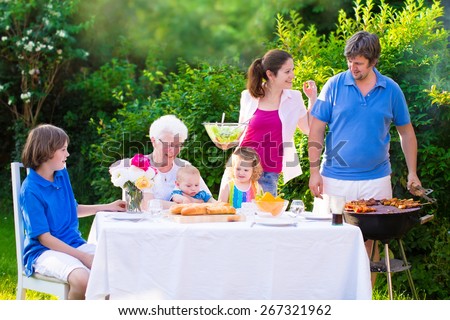Grill barbecue backyard party. Happy big family, mother, father, teen son, cute toddler daughter and little baby, enjoying BBQ lunch with grandmother eating meat in the garden with salad and bread.