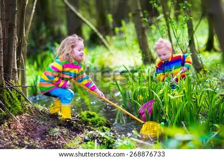 Children playing outdoors. Preschool kids catching frog with net. Boy and girl fishing in forest river. Adventure kindergarten day trip into wild nature, young explorer hiking and watching animals.