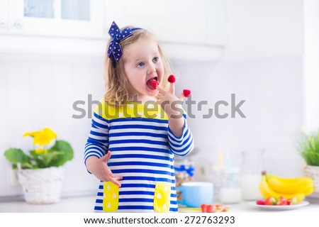 Little girl preparing breakfast in kitchen. Healthy food for children. Child drinking milk and eating fruit. Happy preschooler kid enjoying morning meal, cereal, banana and raspberry. Kids eating.