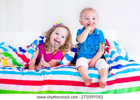 Two kids sleeping in bed under colorful blanket. Children relaxing in bedroom. Tired toddler girl and baby boy before bedtime. Rainbow textile bedding for nursery. Brother and sister play at home.