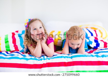 Two kids sleeping in bed under colorful blanket. Children relaxing in bedroom. Tired toddler girl and baby boy before bedtime. Rainbow textile bedding for nursery. Brother and sister play at home.