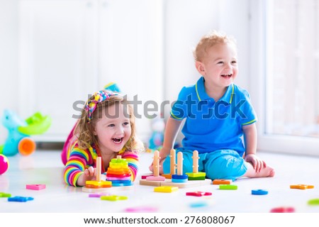 Kids playing with wooden toys. Two children, cute toddler girl and funny baby boy, playing with toy blocks, building towers at home or day care. Educational child toys for preschool and kindergarten.