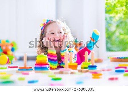 Child playing with wooden toys at preschool. Cute toddler girl having fun with toy blocks, building a tower at home or day care. Educational kids toy for nursery or kindergarten.