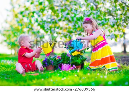 Kids gardening. Children playing outdoors. Little girl and baby boy working in the garden, planting flowers, watering flower bed. Family in blooming fruit tree orchard. Summer vacation on a farm.