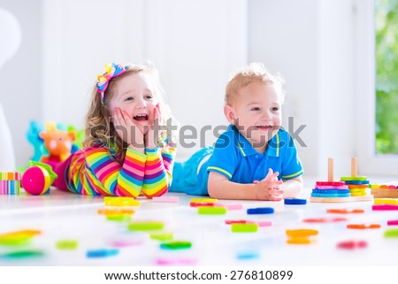 Kids playing with wooden toys. Two children, cute toddler girl and funny baby boy, playing with toy blocks, building towers at home or day care. Educational child toys for preschool and kindergarten.