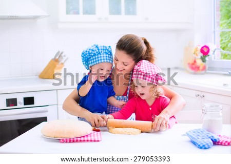 Kids and mother baking. Two children and parent cooking. Little girl and baby boy cook and bake in a white kitchen with modern oven. Brother and sister in chef hats making a pie for dinner.