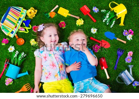 Kids gardening. Children with garden tools. Child with watering can and shovel. Little kid watering flowers. Girl and baby boy relaxing on green backyard lawn in summer.