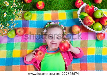 Child eating apple. Little girl playing peek a boo holding fresh ripe apples. Kids eating snack relaxing on a lawn. Children summer fun on a farm picking healthy fruit.
