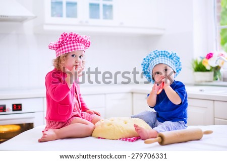 Kids baking. Two children cooking. Little girl and baby boy cook and bake in a white kitchen with modern oven. Brother and sister in chef hats making a pie for dinner.