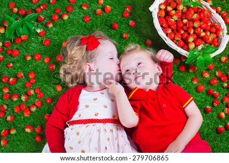 Child eating strawberry. Little girl and baby boy play and eat fresh ripe strawberries. Kids with fruit relaxing on a lawn. Children summer fun on a farm picking berry.