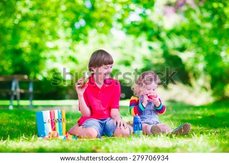 Children in school yard. Kids study. Happy laughing teenager student boy and preschool girl in the school garden reading books and having apple for healthy snack, back to school concept