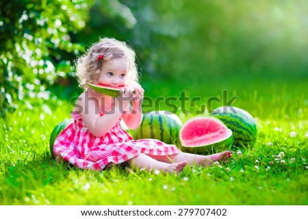 Child eating watermelon in the garden. Kids eat fruit outdoors. Healthy snack for children. Little girl playing in the garden holding a slice of water melon. Kid gardening.