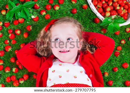 Child eating strawberry. Little girl playing peek a boo holding fresh ripe strawberries. Kids eating fruit relaxing on a lawn. Children summer fun on a farm picking berry.