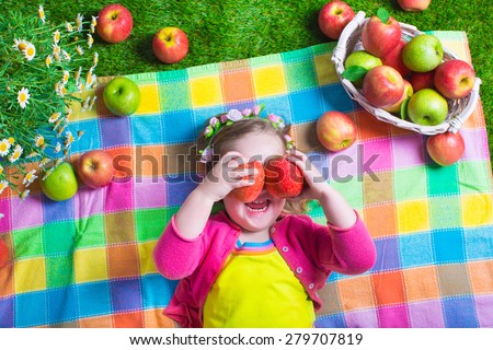 Child eating apple. Little girl playing peek a boo holding fresh ripe apples. Kids eating snack relaxing on a lawn. Children summer fun on a farm picking healthy fruit.