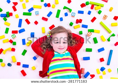 Child playing with colorful wooden toys. Little girl with educational toy blocks. Children play at day care or preschool. Mess in kids room. View from above.