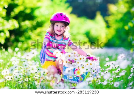 Happy child riding a bike. Cute kid in safety helmet biking outdoors. Little toddler girl on bicycle with daisy flowers in a basket. Healthy preschool children summer activity. Kids playing outside.