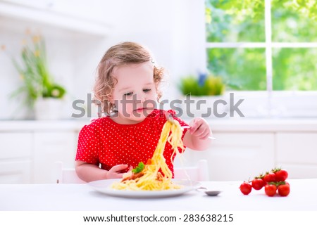 Kids eat pasta. Healthy lunch for children. Toddler kid eating spaghetti Bolognese in a white kitchen at home. Preschooler child cooking noodles with tomato and pepper for dinner. Food for family.