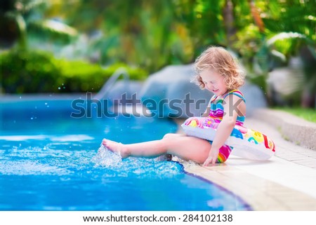 Kids in swimming pool. Children swim outdoors. Toddler child during vacation in a tropical resort with palm trees. Little girl playing on a beach. Active kid in summer with colorful toy floating ring.