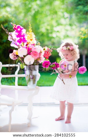 Little girl arranging flowers at home in a vase. Child playing indoors. Kids birthday party. Children giving flower as present. Kid in a living room with big window and door to the garden. Summer fun.