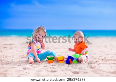 Kids play on a beach. Children building sand castle on tropical island. Summer water fun for family. Boy and girl with toy buckets and spade at the sea shore. Ocean vacation with baby and toddler kid.