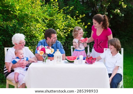 Big family with children have lunch outdoors. Parents with 3 kids and grandmother eat in the garden. Picnic for mother, father, baby boy, toddler girl and teenager child. Generations and retirement.