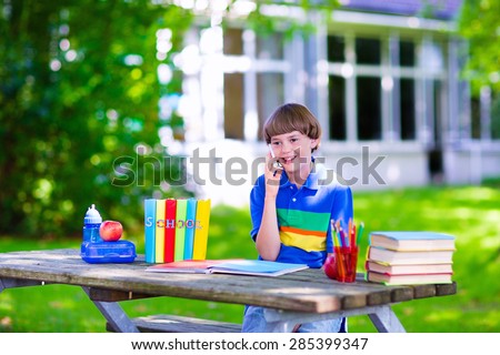 Child in school with telephone. Smart teenager boy studying and learning outdoors, reading books. Children calling, texting with smartphone. Kids talking on the phone. Students with modern gadgets.