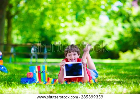 Child in school with tablet PC. Smart teenager student boy studying and learning outdoors, reading books. Children doing homework research on the internet with modern computer. Kids with gadgets.