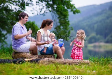 Family on summer hike. Young parents with kids hiking next to a lake. Mother, father and two children having picnic outdoors. Active trekking with baby and toddler. Beautiful nature of Germany.