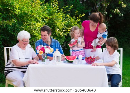 Big family with children have lunch outdoors. Parents with 3 kids and grandmother eat in the garden. Picnic for mother, father, baby boy, toddler girl and teenager child. Generations and retirement.