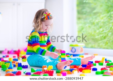Preschooler child playing with colorful toy blocks. Kids play with educational toys at kindergarten or day care. Preschool children build tower with plastic block. Toddler kid in nursery.