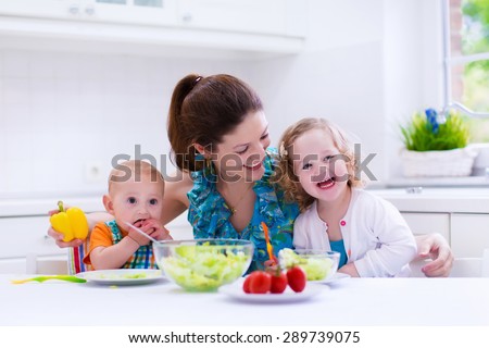 Young mother and two children cooking in a kitchen. Parent and kids cook dinner. Family with baby and toddler kid eat at home. Child preparing and eating vegetable lunch. Preschooler healthy nutrition