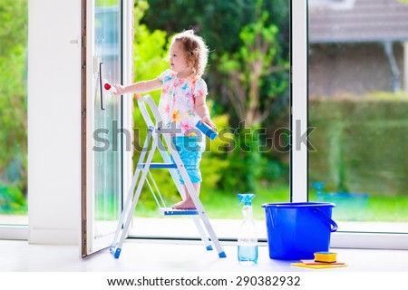 Little girl washing a window. Kids clean the house. Children help at home. Toddler kid cleaning windows and doors standing on a ladder. Child helping with housework holding sponge and soap bottle.