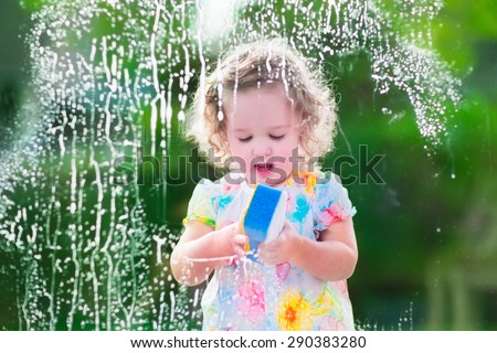 Little girl washing a window. Kids clean the house. Children help at home. Toddler kid cleaning windows and doors standing on a ladder. Child helping with housework holding sponge and soap bottle.