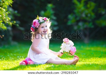Little cute girl with pink flowers. Child wearing a white dress playing in summer garden. Kids gardening. Children play outdoors. Toddler kid with flower bouquet for birthday or mother\'s day.