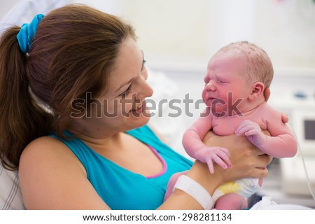 Mother giving birth to a baby. Newborn baby in delivery room. Mom holding her new born child after labor. Female pregnant patient in a modern hospital. Parent and infant first moments of bonding.