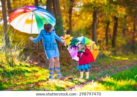 Mother and daughter play in autumn park with golden leaves. Child holding umbrella in the rain. Parent and kid walk in the forest on a rainy fall day. Children playing outdoors with yellow maple leaf