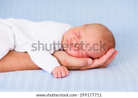 Newborn baby sleeping in arms of his father. Dad holding new born son. Child taking a nap on parent hand. Infant kid sleeping on a blue blanket. Textile bedding for kids. Parents and children bonding.