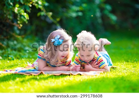 Kids reading a book in summer garden. Children study. Boy and girl play in school yard. Preschool friends playing and learning. Siblings doing homework. Kindergarten kid and toddler read books.