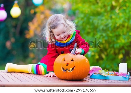 Little girl carving pumpkin at Halloween. Dressed up child trick or treating. Kids trick or treat. Child in witch costume playing in autumn park. Toddler kid with jack-o-lantern.