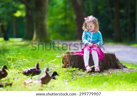 Little girl feeding duck in a summer park. Children feed birds and animals. Child playing outdoors. Kids play in sunny autumn forest. Toddler kid watching wild bird. Preschooler exploring nature.