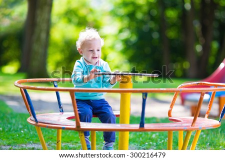 Little boy on a playground. Child playing outdoors in summer. Kids play on school yard. Happy kid in kindergarten or preschool. Children having fun at daycare play ground. Toddler on a swing.