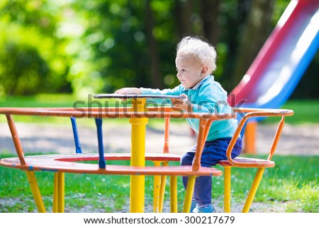 Little boy on a playground. Child playing outdoors in summer. Kids play on school yard. Happy kid in kindergarten or preschool. Children having fun at daycare play ground. Toddler on a swing.