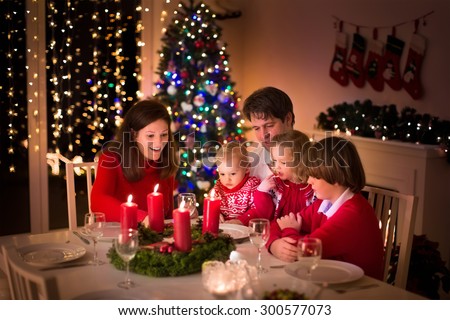 Big family with three children celebrating Christmas at home. Festive dinner at fireplace and Xmas tree. Parent and kids eating at fire place in decorated room. Child lighting advent wreath candle.
