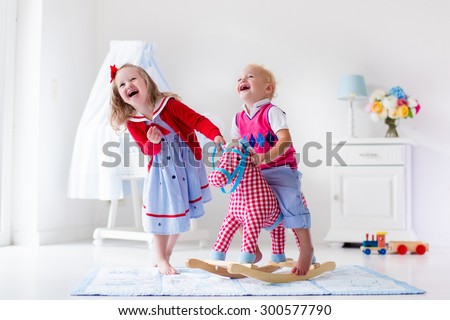Two children play indoors. Kids riding toy rocking horse. Boy and girl playing at day care or kindergarten. Beautiful nursery for baby and toddler. Toys for preschool child. Brother and sister at home