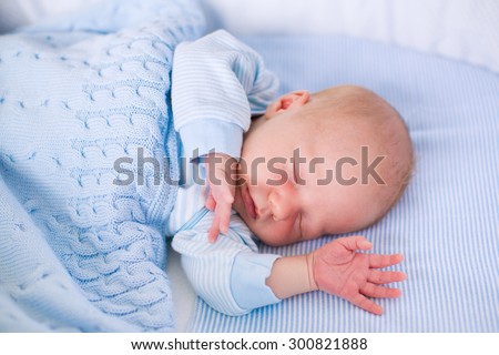 Newborn baby boy in bed. New born child sleeping under a blue knitted blanket. Children sleep. Bedding for kids. Infant napping in bed. Healthy little kid shortly after birth. Cable knit textile.