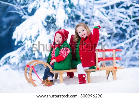 Little girl and baby boy enjoying a sleigh ride. Child sledding. Toddler kid riding a sledge. Children play outdoors in snow. Kids sled in snowy park. Outdoor winter fun for family Christmas vacation.