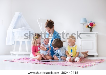 Mother and children play indoors. Family with kids in a white bedroom. Mom with baby, boy and girl playing and reading books at home. Beautiful nursery for baby and toddler. Room for preschool child.