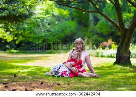 Grandmother and granddaughter enjoying picnic in a park. Grandma playing with little toddler girl in a sunny autumn forest. Summer outdoor fun in the garden. Grandparents and kids on a meadow.